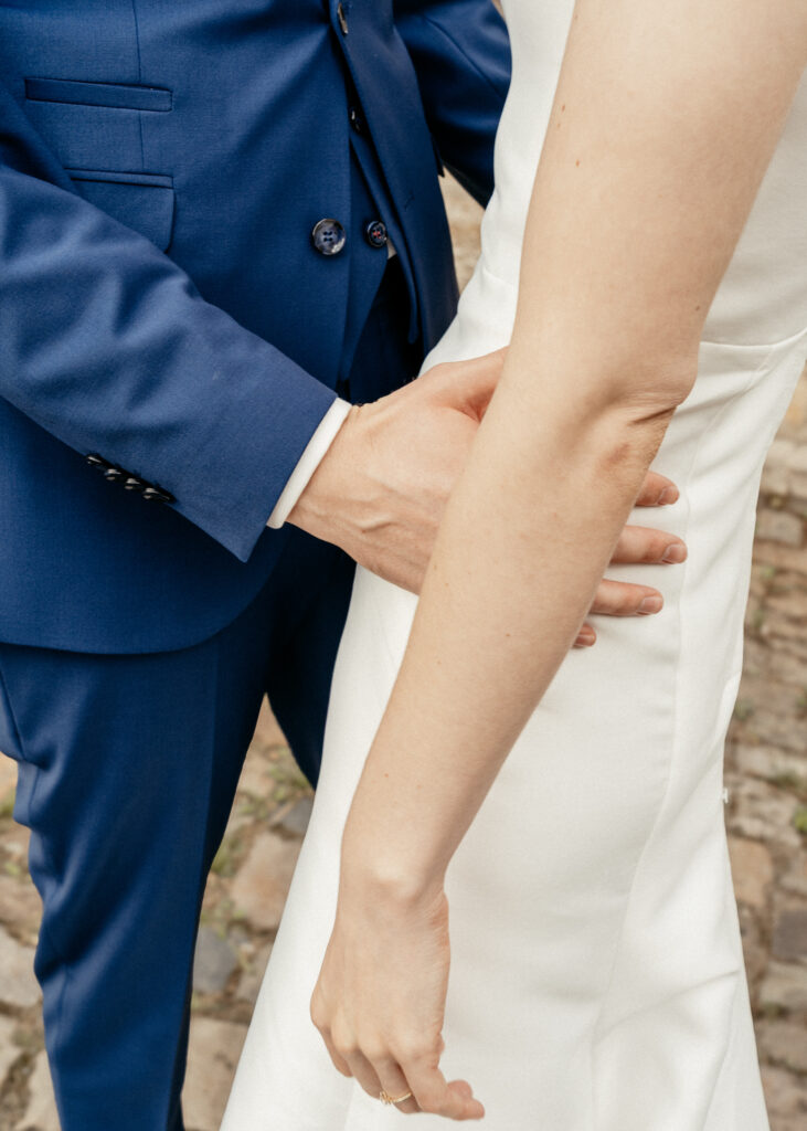 Detailaufnahme von Bräutigam im blauen Anzug, der seine Hand an die Taille der Braut legt, Hochzeitsfotografie von emilys stories