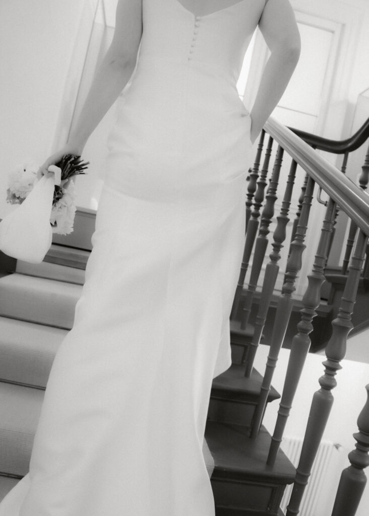 Braut im schlichten brautkleid geht eine treppe hinauf, rueckenansicht, schwarz-weiss-hochzeitsfotografie von emilys stories